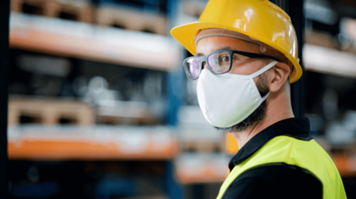 Close-up of a male worker wearing a yellow safety vest, helmet, goggles and mask