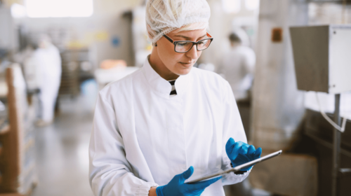 Female worker wearing lab coat, gloves and a tablet in food factory